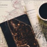 Hartă, carnet cu notițe, pașaport și o cană de cafea pe o masă, pregătite pentru planificarea unei călătorii