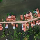 Case de lemn pe piloni deasupra unui lac, cu bărci tradiționale legate între ele la apus